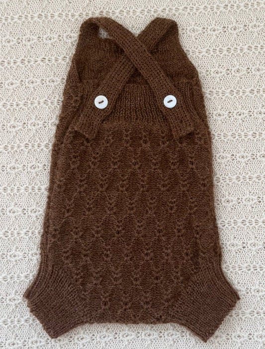 Chocolate alpaca newborn baby romper with a textured knit pattern and two white buttons, laid flat on a cream-colored lace background.