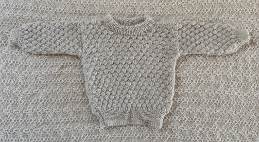A ivory -knit baby sweater laid flat on a matching textured knit blanket background.